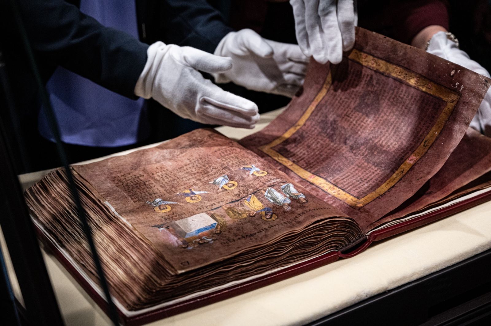 Mani in guanti bianchi girano con cura una pagina di porpora del Codex