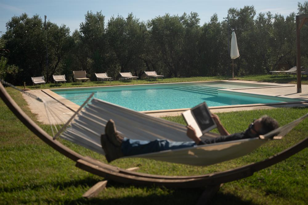 Un uomo legge in un'amaca davanti alla piscina