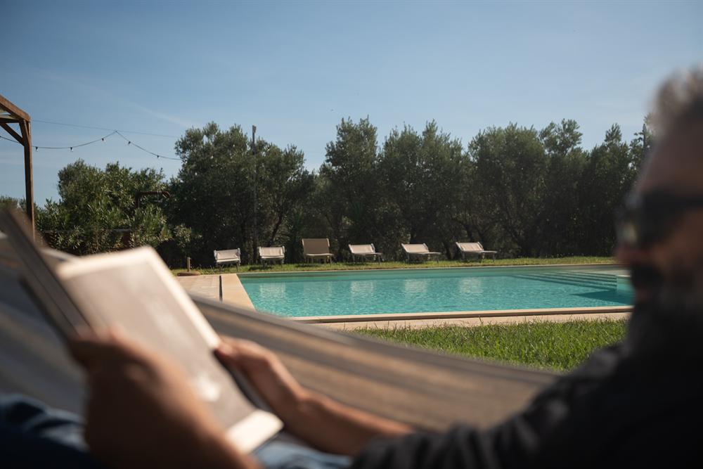 La piscina vista da un'amaca, con lettini e ulivi sullo sfondo