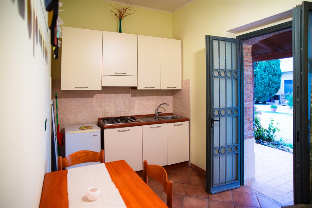 Un angolo cottura con frigorifero e tavolo, e la porta aperta sul cortile
